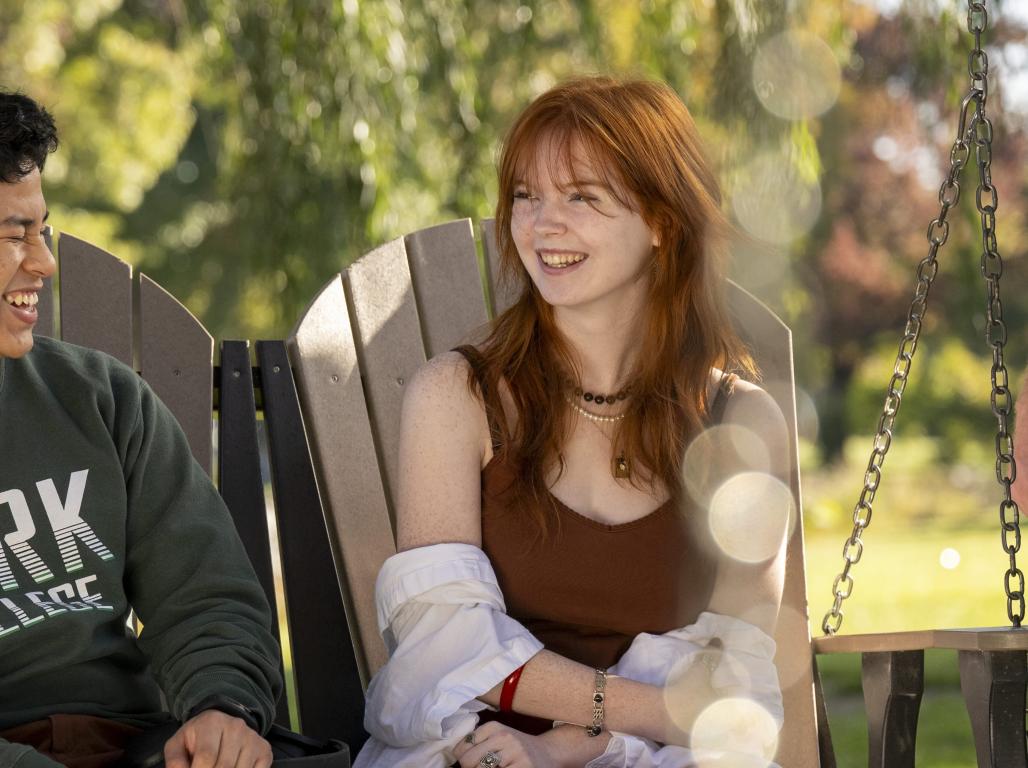 Students laughing and smiling on a bench swing with willow branches visible in the background.