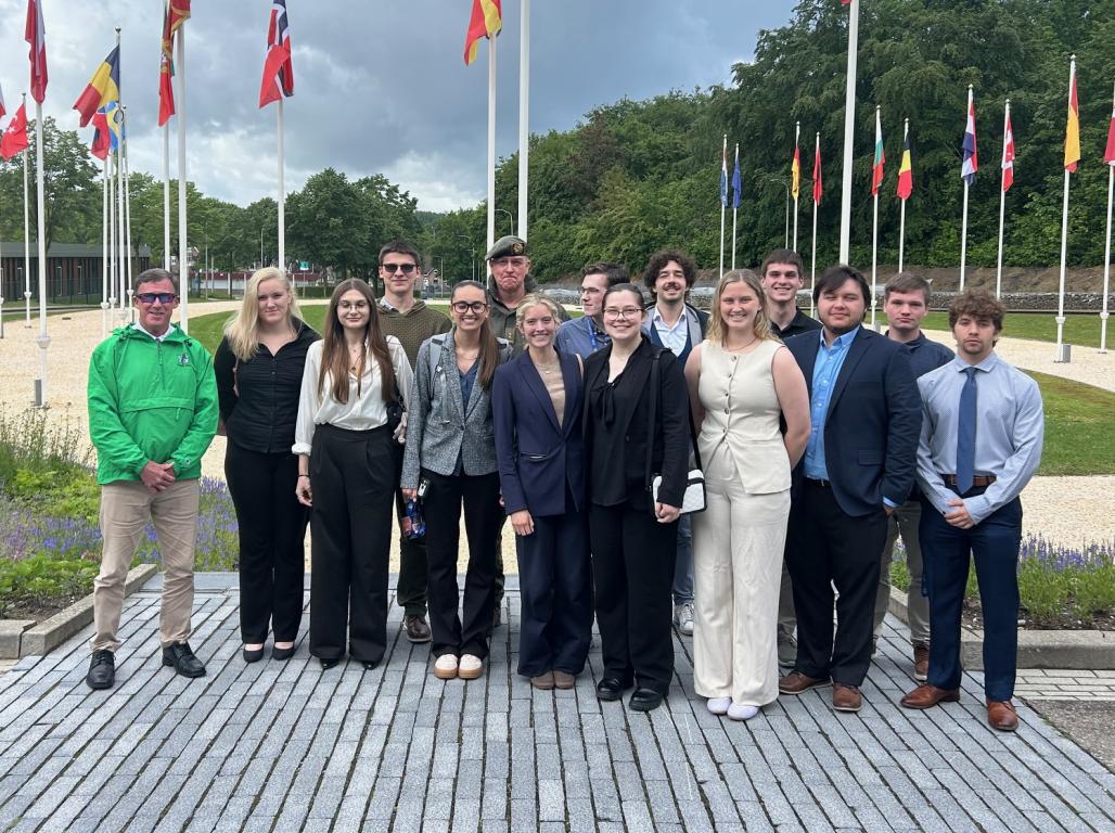 A group of students pose for a photo outside in front of a circle of international flags.