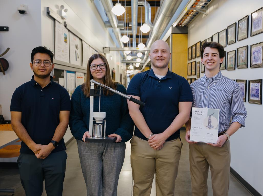 Four York College Mechanical Engineering students stand with their completed class project, with Aidan Heck ’27 at right holding the project poster.