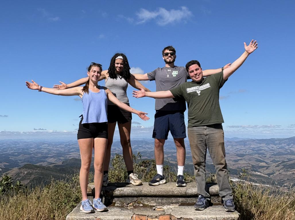 Four students standing on mountain top with their arms in the air in Brazil.