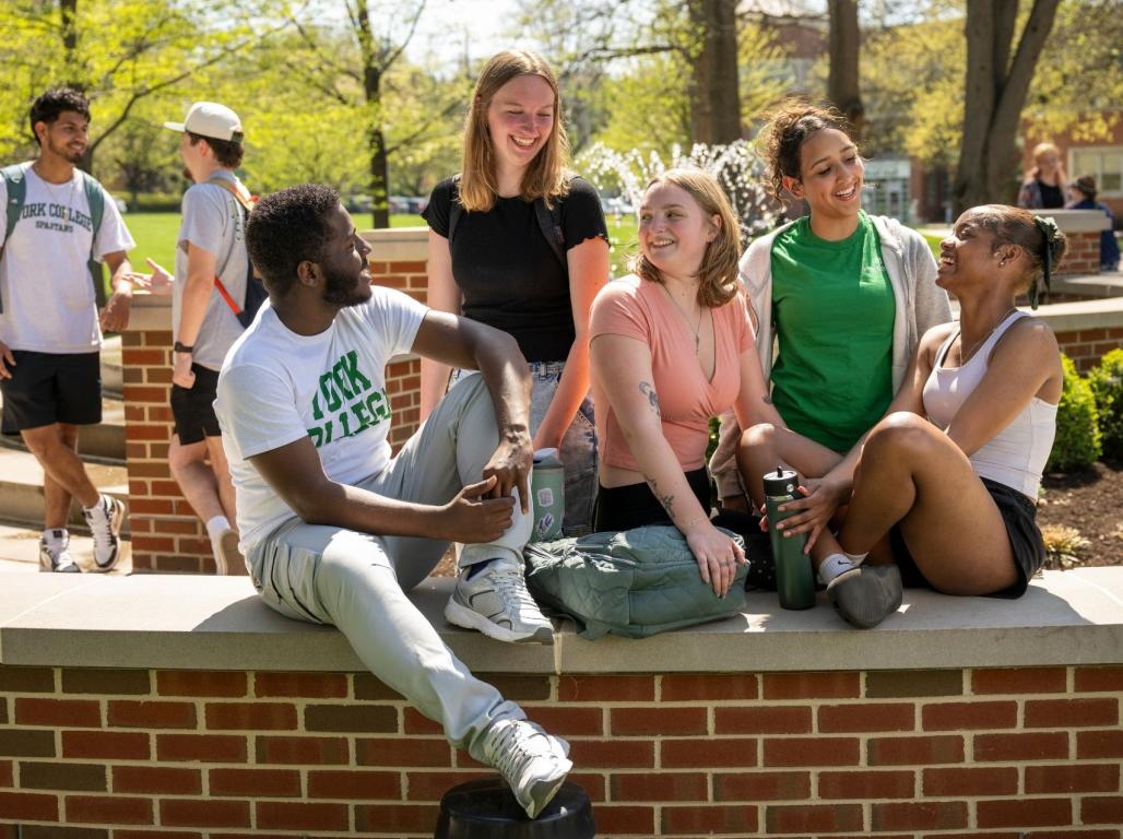 York College students talk and laugh together while sitting beside a campus fountain.