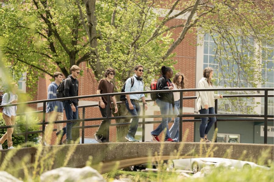 A group of students walks across the bridge over the campus creek. 