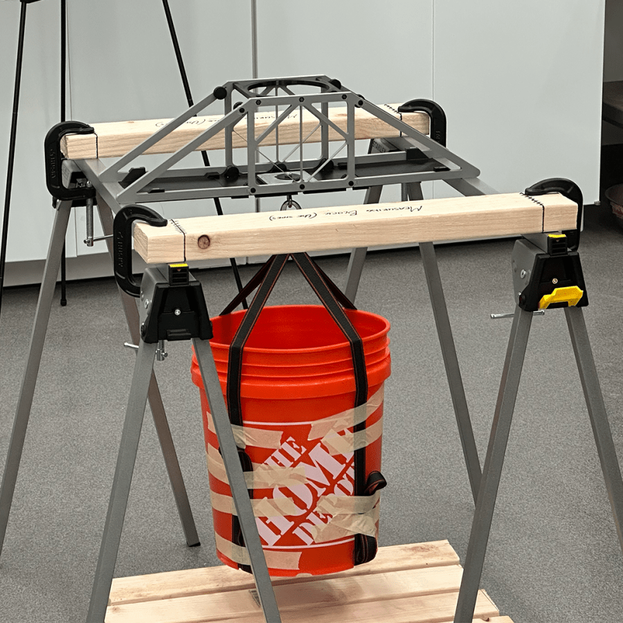 The strength of a 3D printed bridge is tested by weight added to a bucket that's fastened to the center.