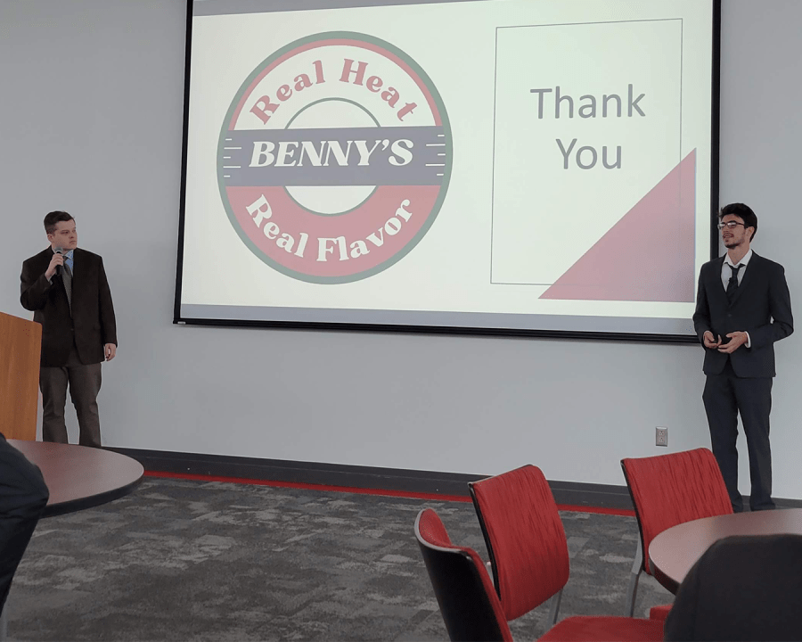 Two people in business suits giving a presentation in front of a projection screen that says "Real Heat, Real Flavor."