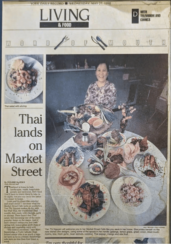 An old newspaper article with the headline "Thai lands on Market Street," and a photo of a person happily presenting an assortment of dishes on a table.