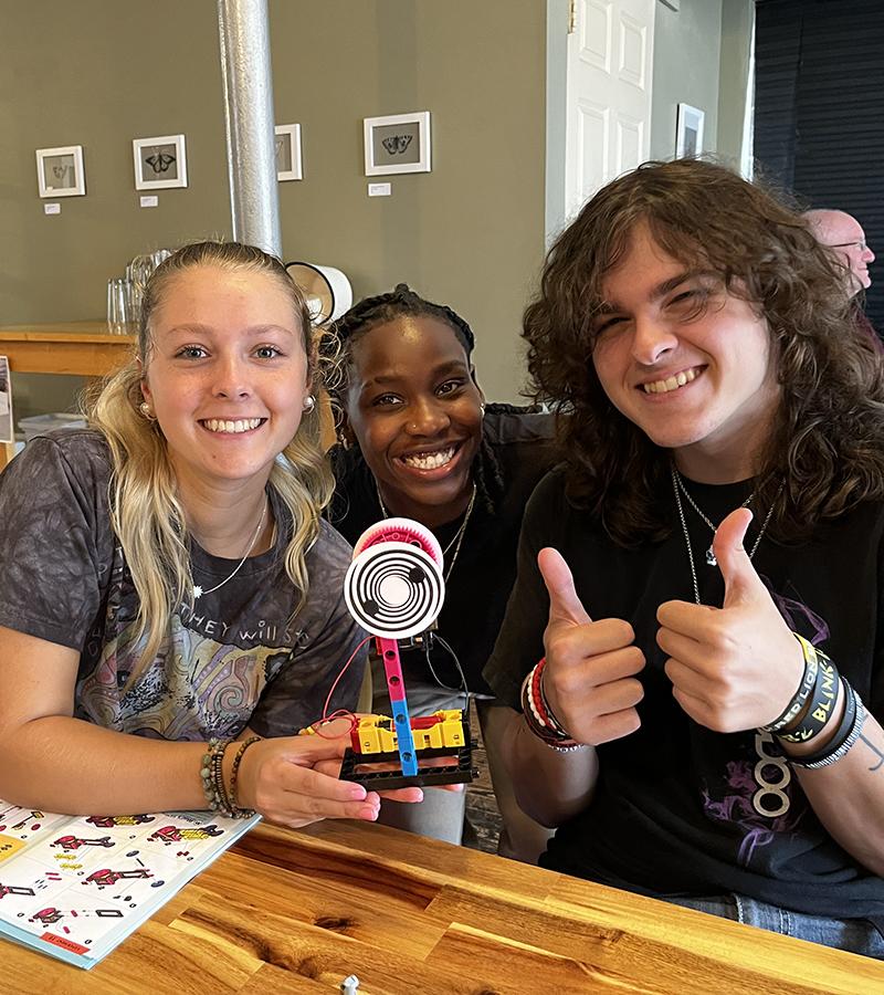 Three student pose and smile with a lego creation