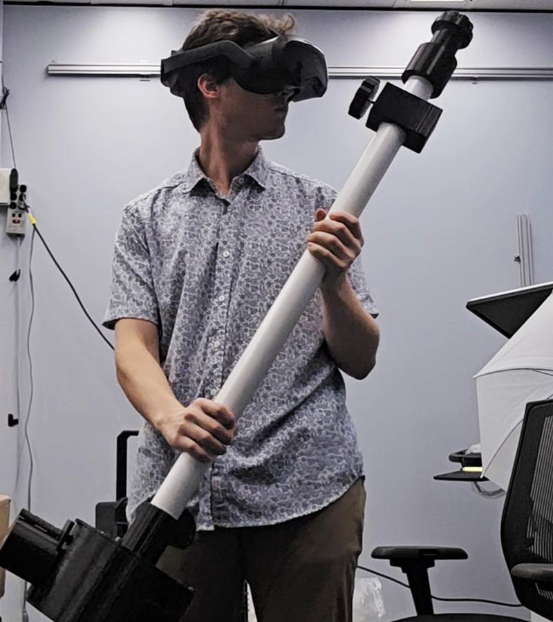 Josh Polancheck at NASA with VR goggles on holding a large instrument
