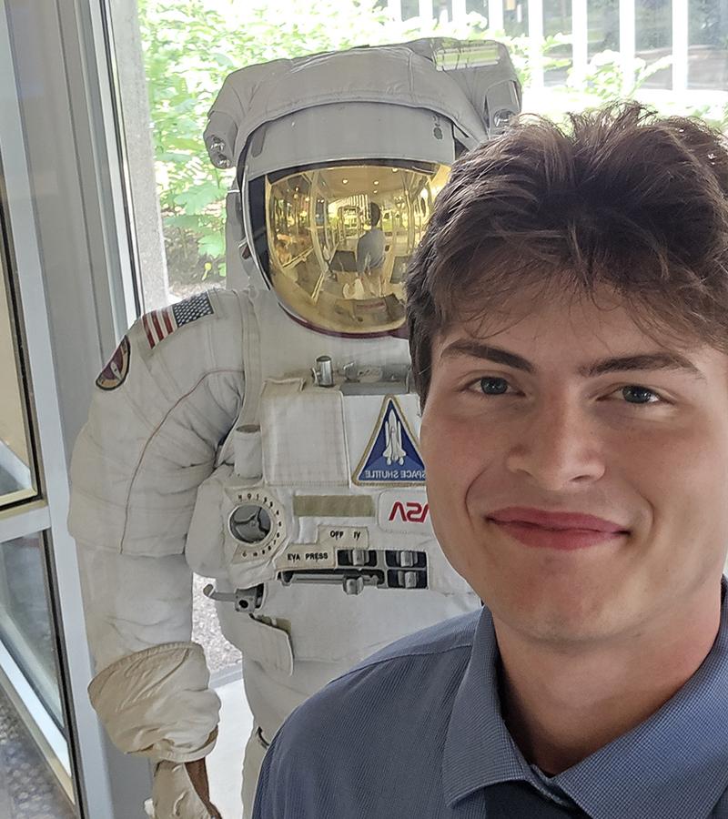 Josh Polancheck at NASA with a space suit behind him