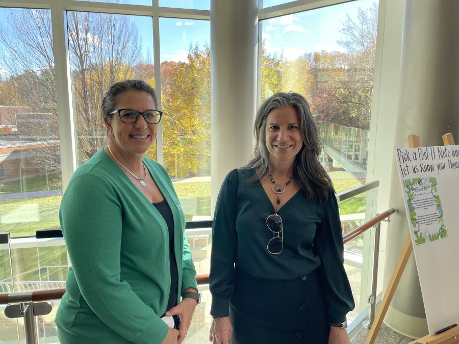 Two individuals smiling at the camera in a room with large windows.