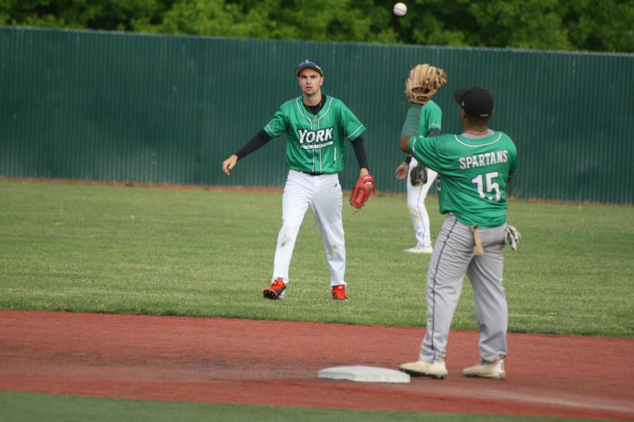 Baseball players wearing green York College Spartan jerseys tossing a baseball on a baseball field.