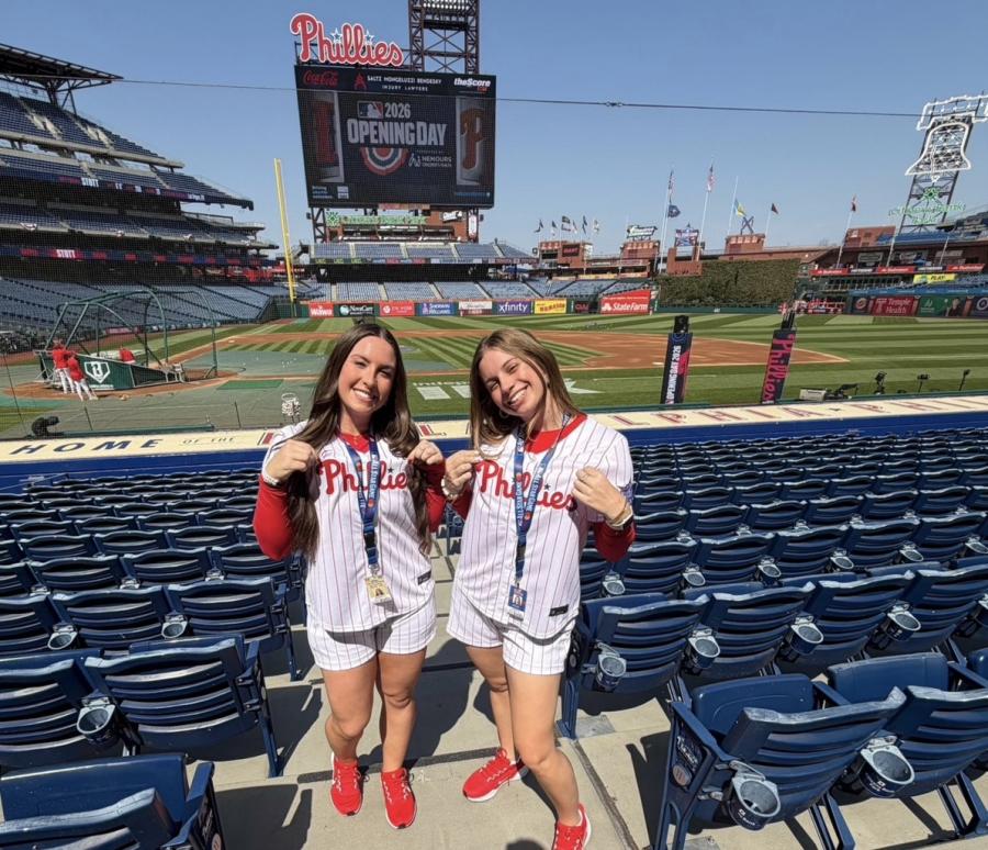 Two people showing off their Phillies jerseys while standing among the empty seats of the Philadelphia Phillies stadium.
