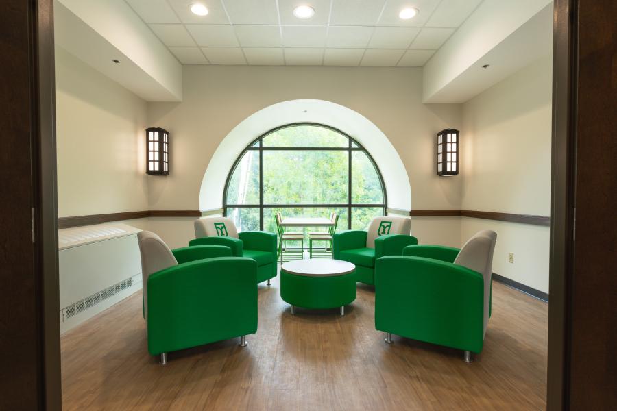 Sitting area with green chairs and a circular window