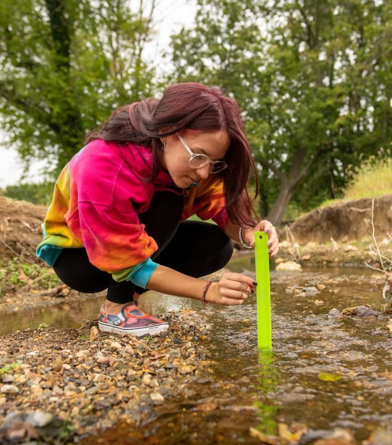 A student is crouching taking measurements in a creek