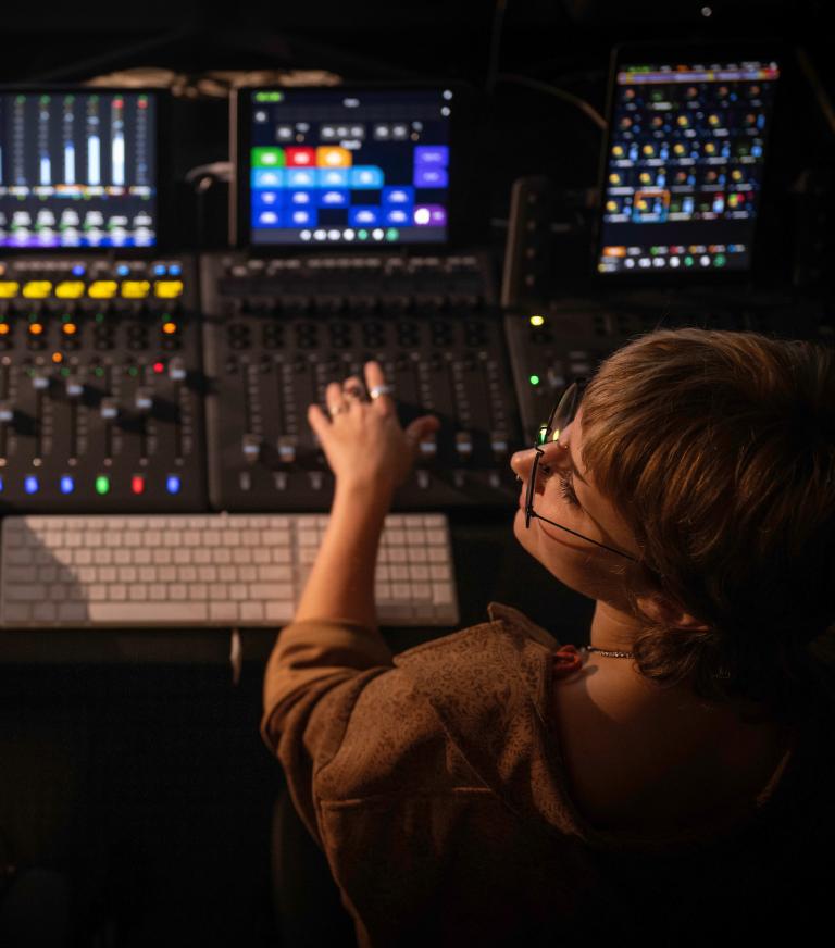 A student and instructor sit before an audio mixer with hands on the slider control knobs.
