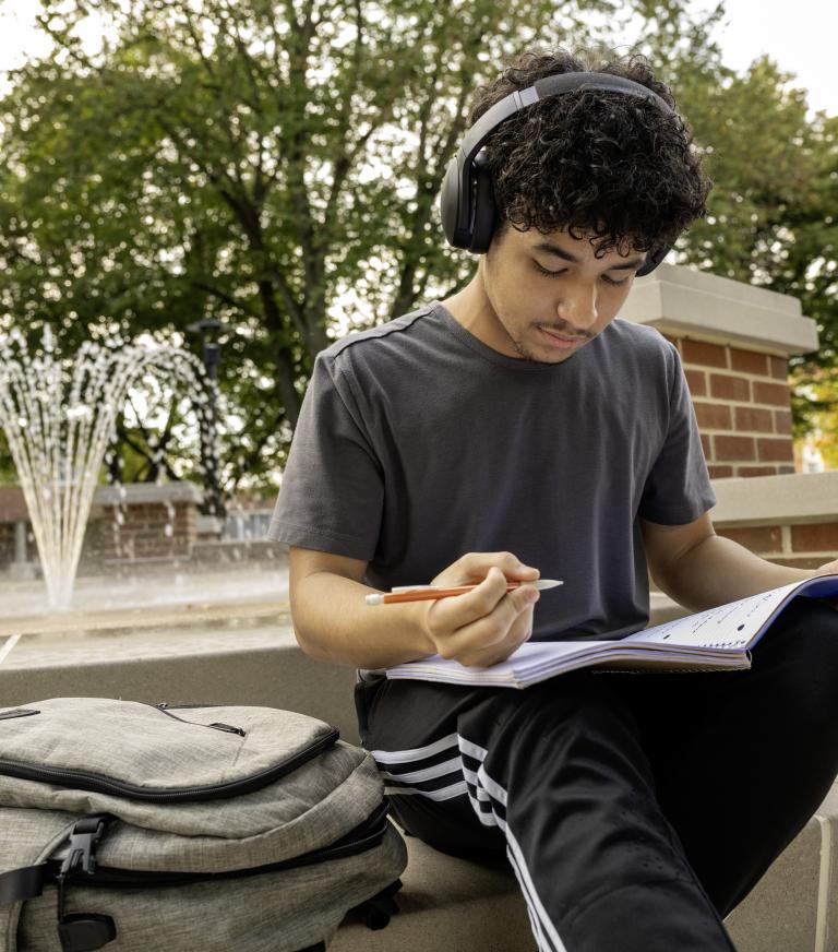College student studying outdoors with a fountain in the background.