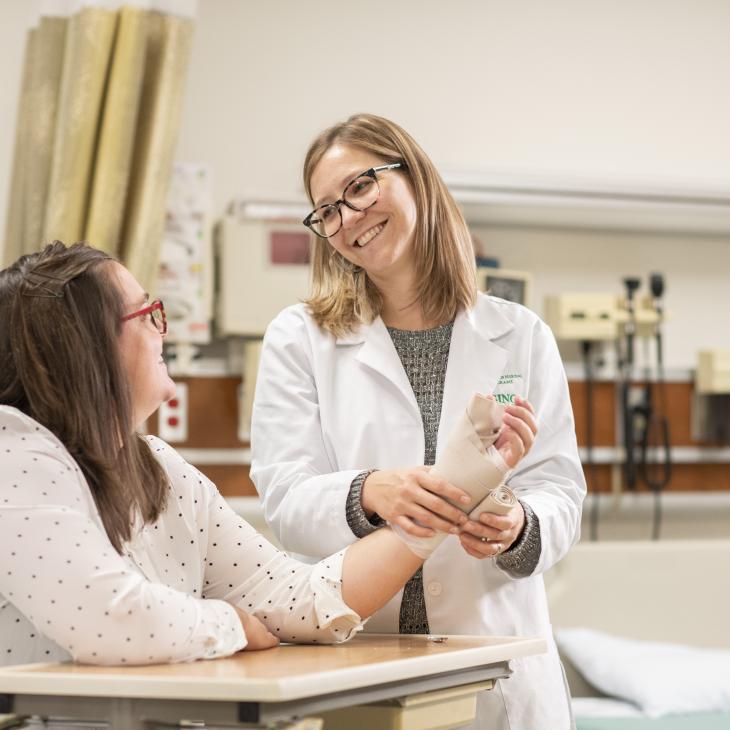 A student nurse helping a patient get her wrist wrapped.