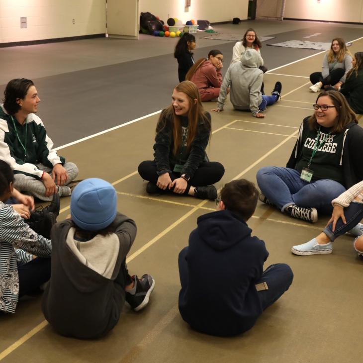 Groups of students sit in circles on a gymnasium floor smiling and talking