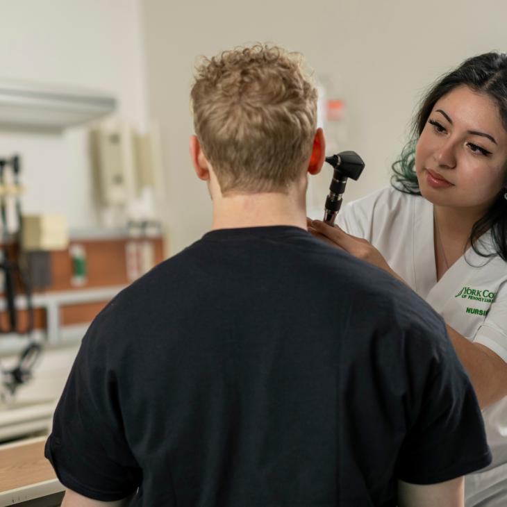 A nursing student uses an otoscope to examine another student's ear.