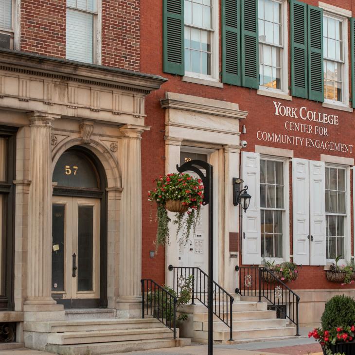 The York College Center for Community Engagement is pictured. It is a brick building with green and white shutters and flower boxes on the first floor windows.