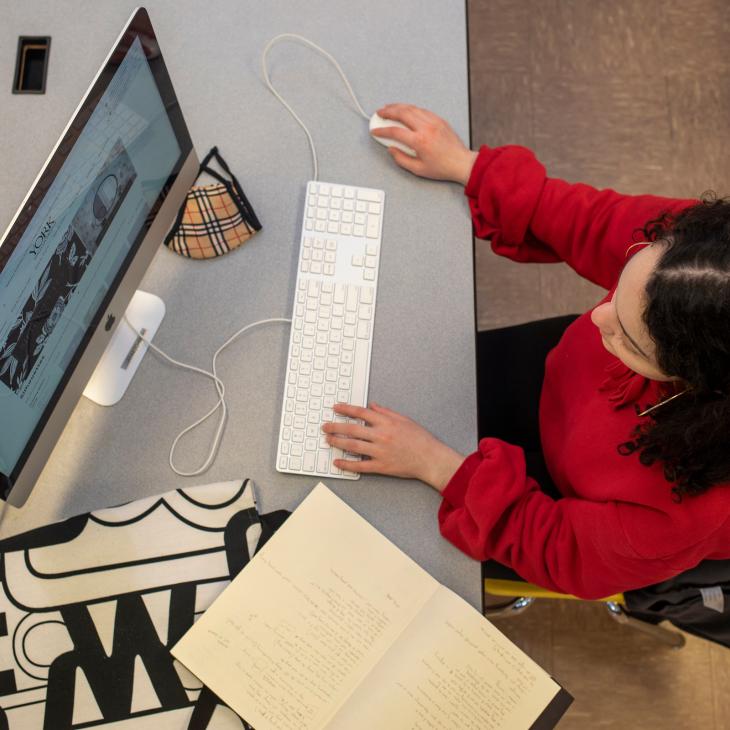 A student works on a computer displaying images of art with an open notebook next to the keyboard.