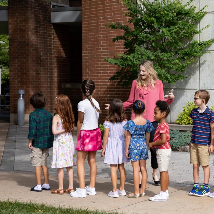 A teacher stands amidst a small group of young children on the grounds of York College. 