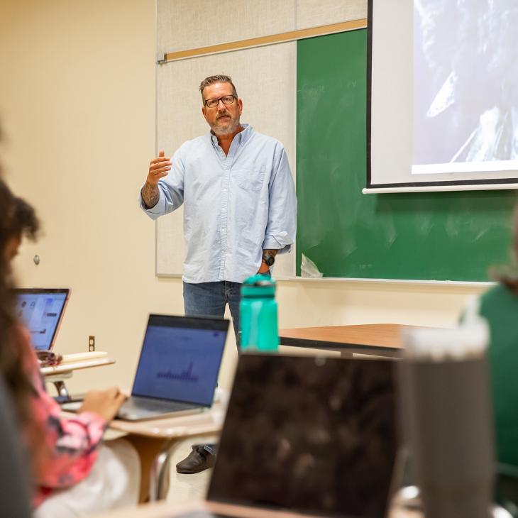 A history professor standing in front of the classroom teaching a group of students.