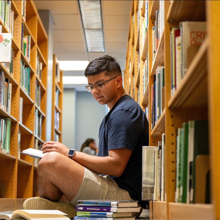 Student sitting on the floor in the library reading books