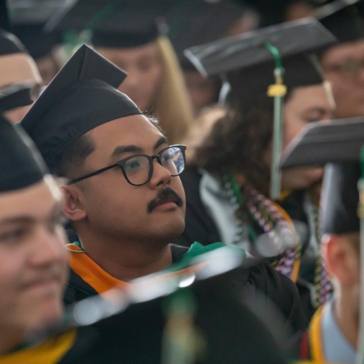 A graduating student wears a cap and gown as he sits in the crowd on graduation day.