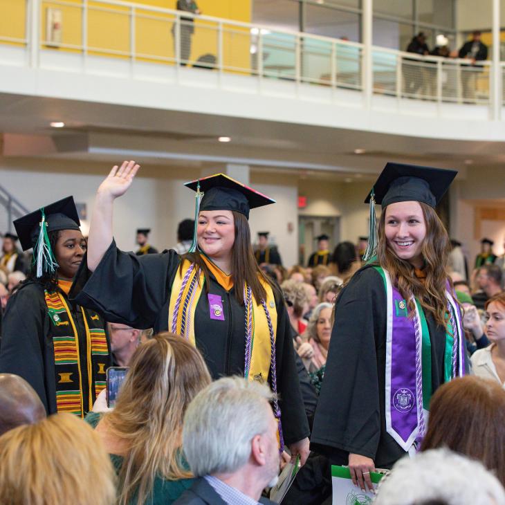 A graduating student waves in her regalia during the processional at Commencement.