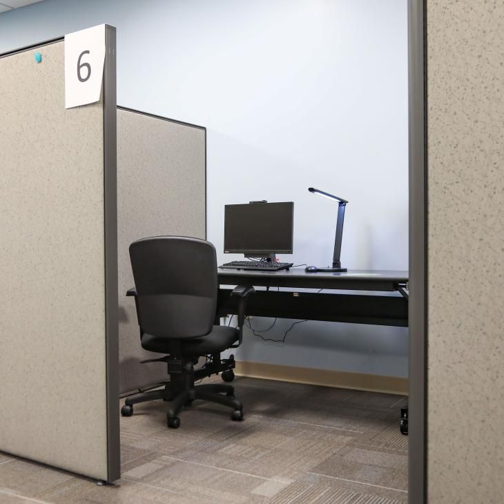 A cubicle in the Testing Center provides an individual seating area with a comfy office chair, desk lamp, and desktop computer.