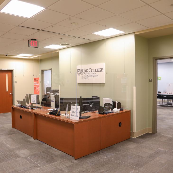 The lobby of the YCP Testing Center with two large adjoining reception desks in front of the wall separating the lobby from the testing center desks. There are two doors to the testing center on each side of the reception desks.