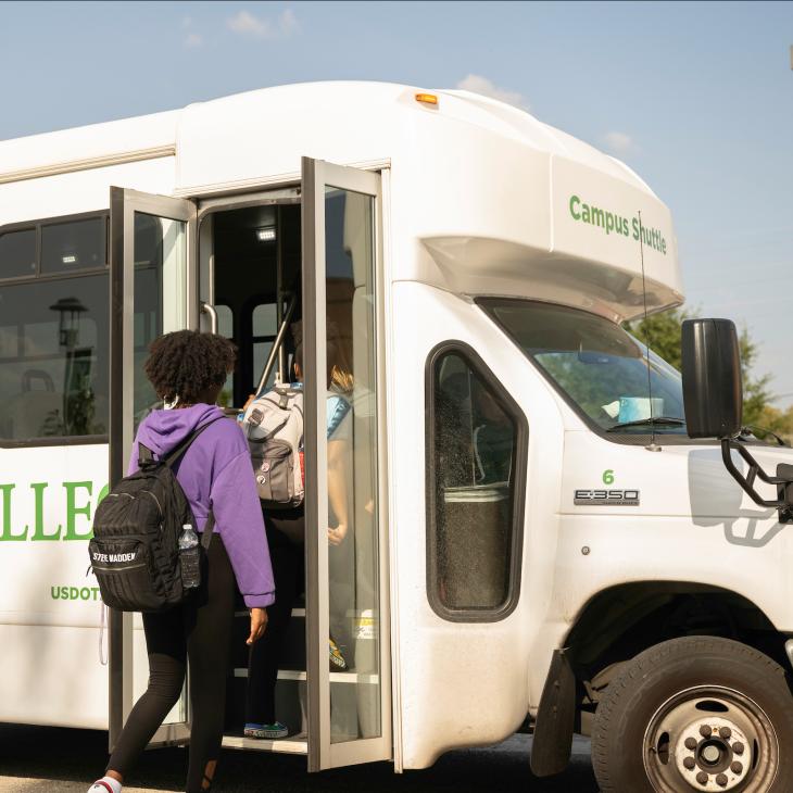 A student steps on board a campus shuttle bus. 