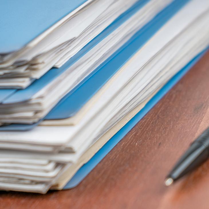 A stack of blue folders filled with documents rests on a table. An open is to the right of the folders.