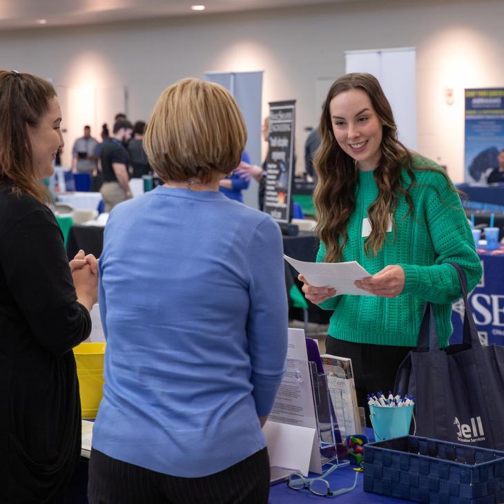 An employer chats with two students at her company's career expo table.