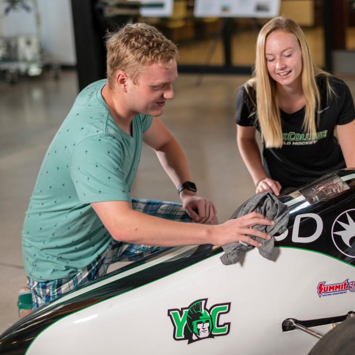 Two students wipe down the exterior of a YCP Formula SAE racecar in the Kinsley Engineering Center.