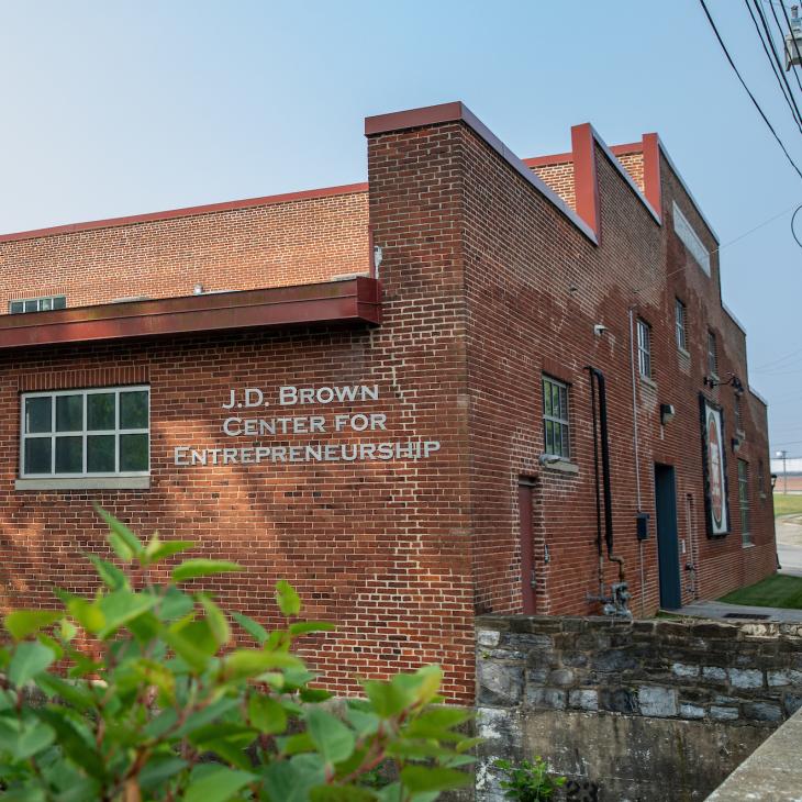 An industrial red brick building is lined with greenery. Signage reads Kings Mill Deport and J.D. Brown Center for Entrepreneurship