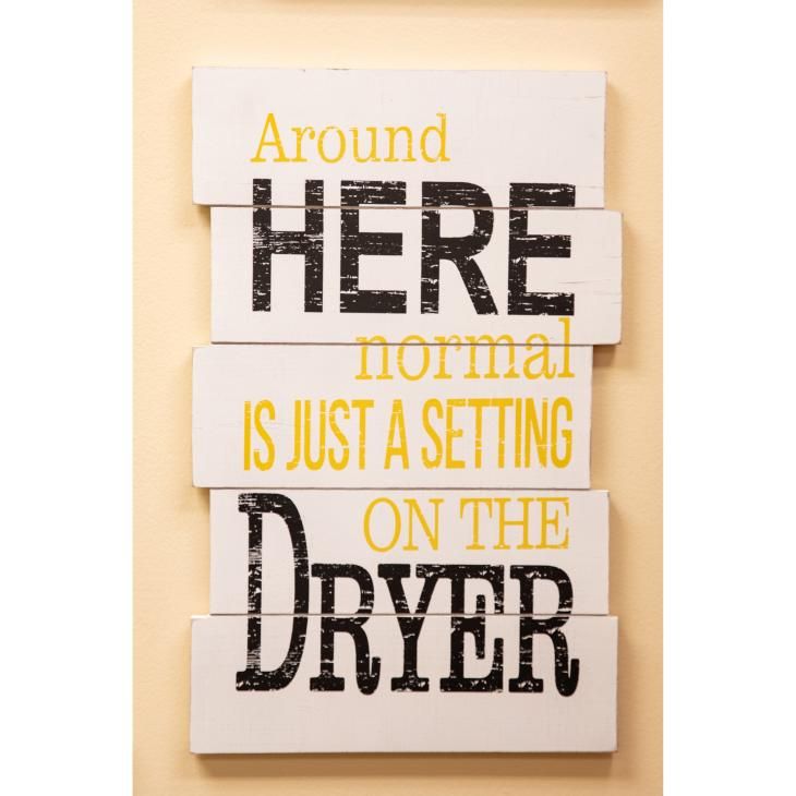 A wall hanging of painted boards of uneven lengths. The message "Around HERE normal is just a setting ON THE Dryer" is painted in yellow and black in varied fonts.