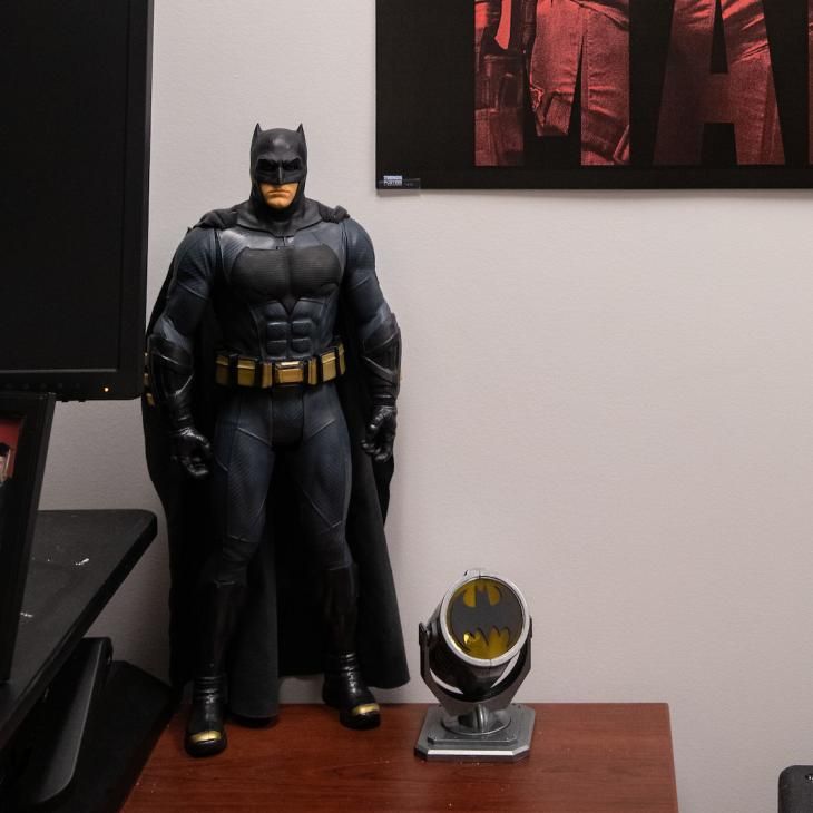 A Batman figurine sits on an office shelf and a Batman poster hangs on the wall above it.