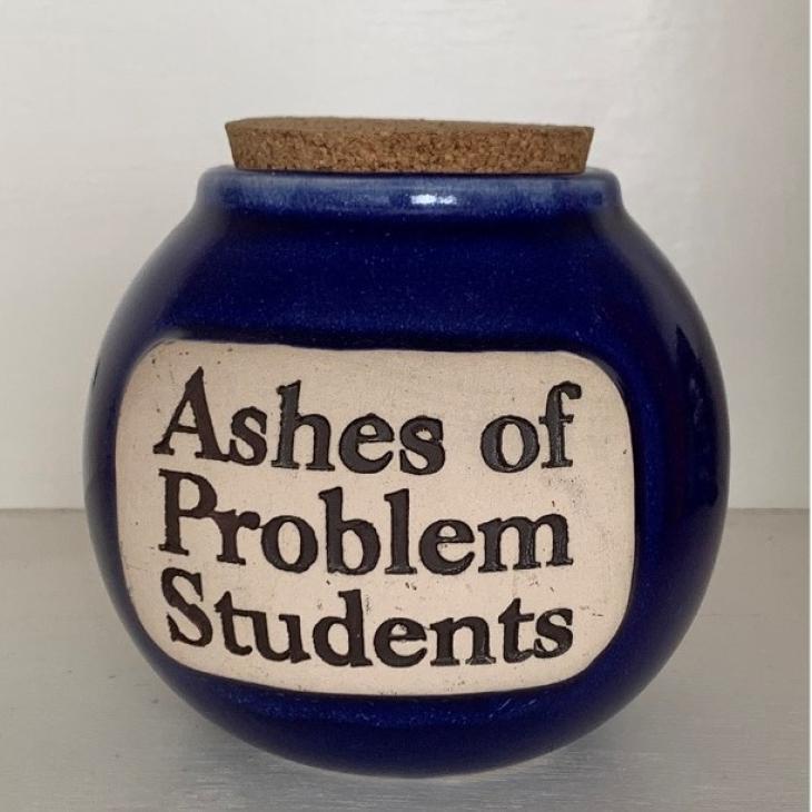 A dark colored round jar with a cork lid. The label on the jar reads, "Ashes of Problem Students."