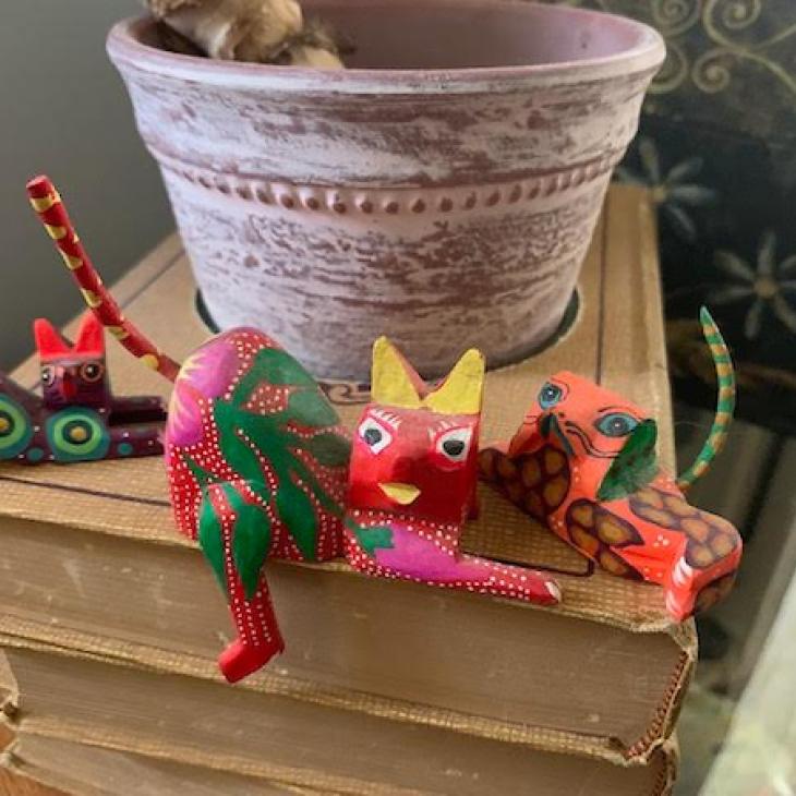 A pink and green piece of Mexican folkart shaped like a cat sits on a corner desk.