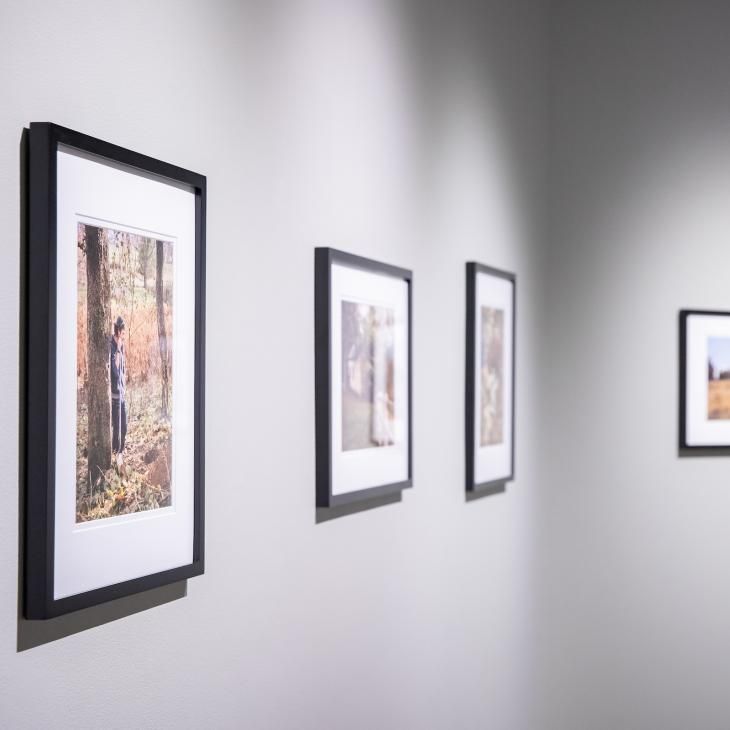 The gallery wall at a York College faculty art exhibition features several framed art prints and photographs.