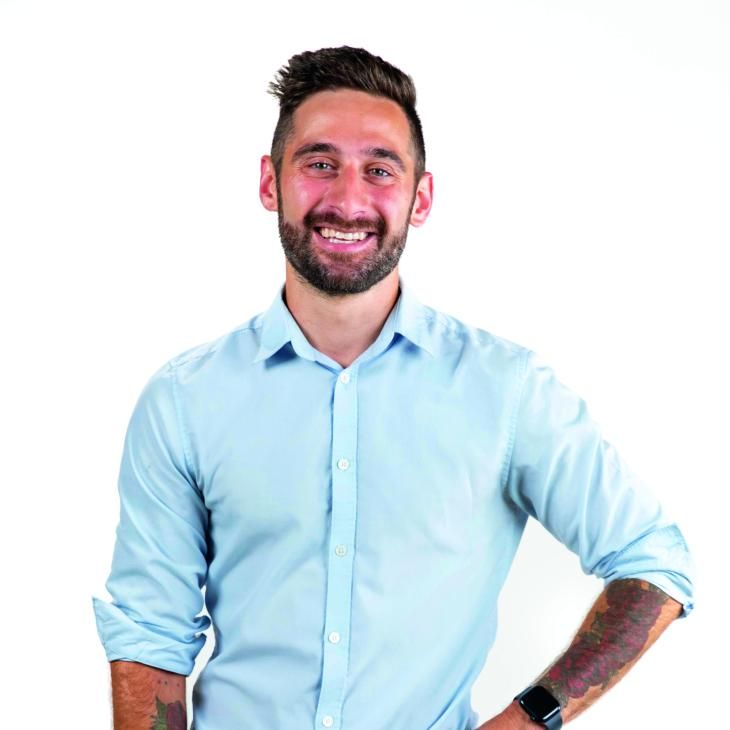 A portrait of John Gaeta, standing business-casual and confident in front of a white backdrop.