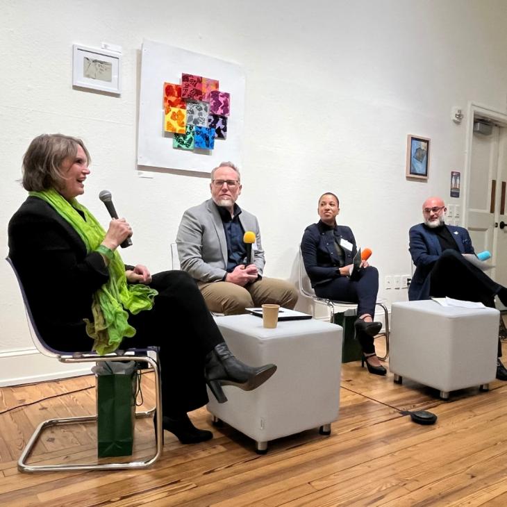 Panel of four speakers seated indoors, engaged in discussion during a campus event.
