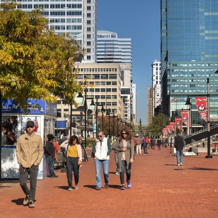 People walking down the sidewalk in Baltimore City on a sunny day.