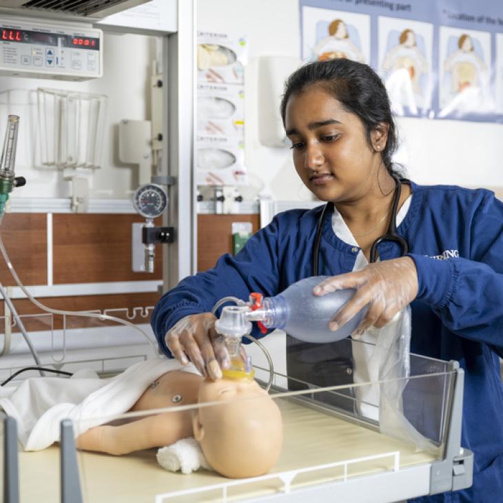 A nursing student practices CPR on an infant mannequin.