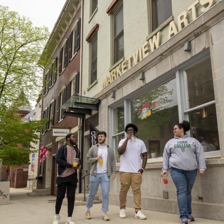 A group of individuals smile while walking outside a building with a "Marketview Arts" sign.