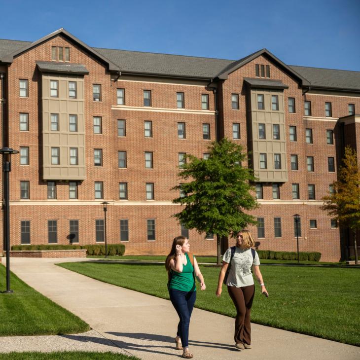 Two people walking away from a large housing building on a sunny day.
