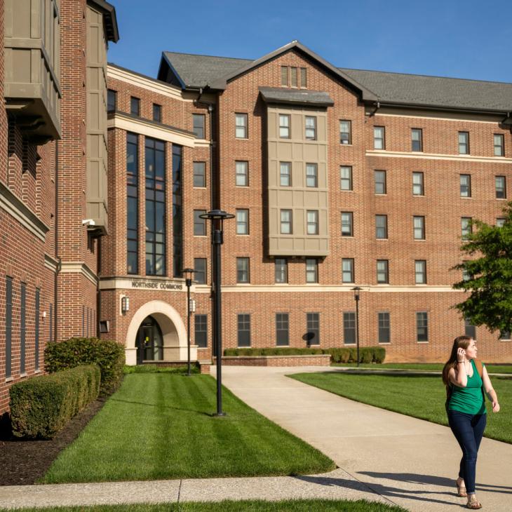 Two people walking away from a large housing building on a sunny day.