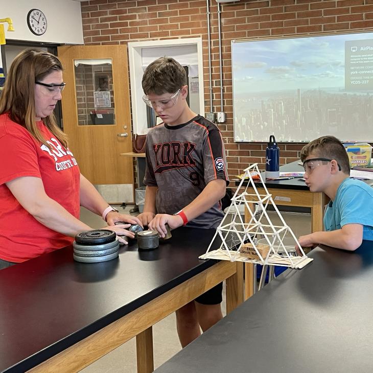 Two students work with a teacher on a popsicle stick bridge