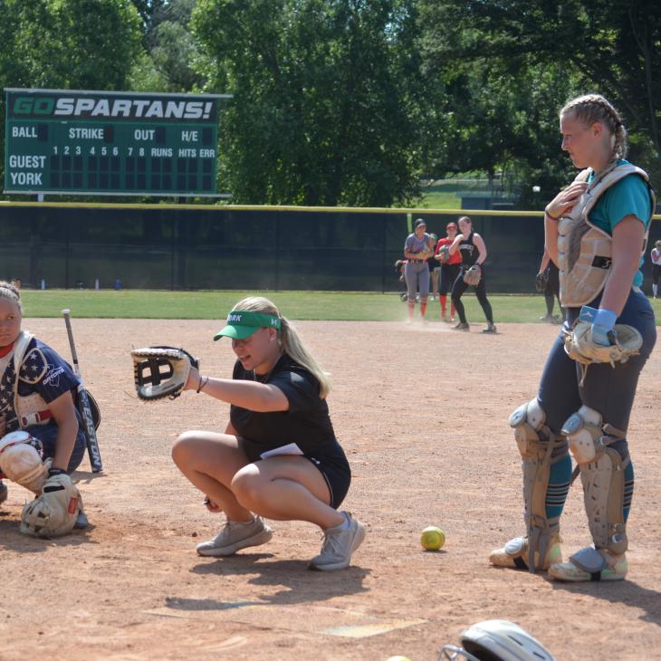 A group of students and a teacher crouch down in catching gear for softball practice